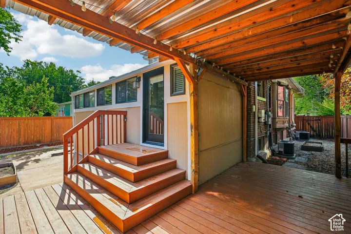 Expansive wood-finish decking with a covered patio area, featuring a slatted wood ceiling, and a multi-level staircase with wood railings