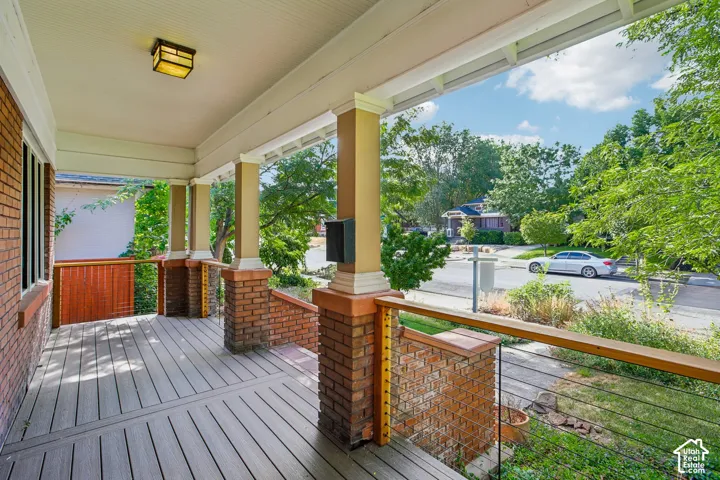 Inviting front porch featuring substantial brick pillars, a wood-finish deck, and a modern cable railing system