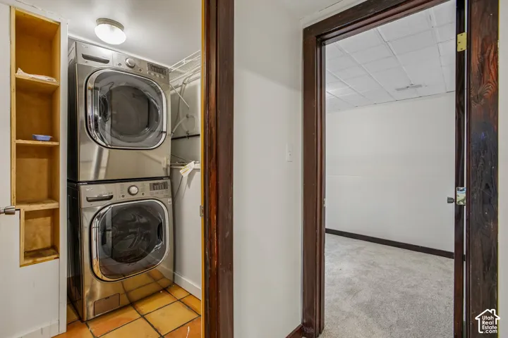 Stacked laundry appliances with a tile floor and adjacent built-in shelving