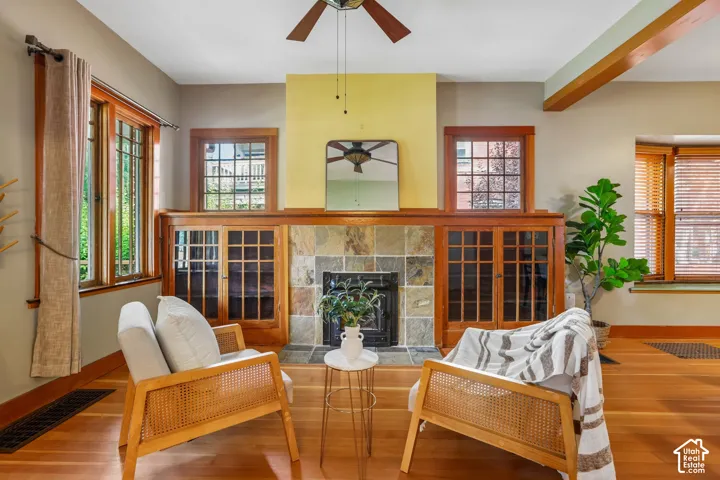 Hardwood flooring, wood-framed windows, stone-tile fireplace surround, built-in cabinetry, and exposed ceiling beam
