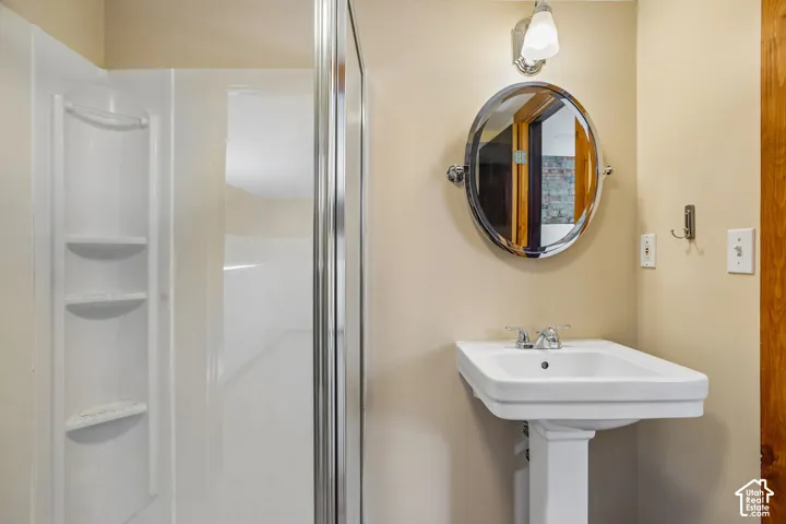 Pedestal sink with chrome faucet, oval mirror, wall-mounted light fixture, and walk-in shower with built-in shelving