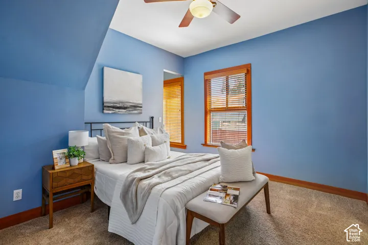 Sloped ceiling with an integrated ceiling fan, window with wood trim and blinds, and carpet flooring