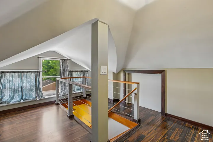 Wood-finish flooring throughout, sloped ceiling, and a modern stair railing with wood and metal elements