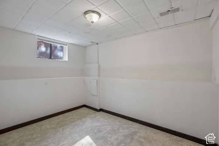 Finished basement room featuring neutral wall paneling, carpeted flooring, recessed ceiling lighting, and a high basement window for natural light
