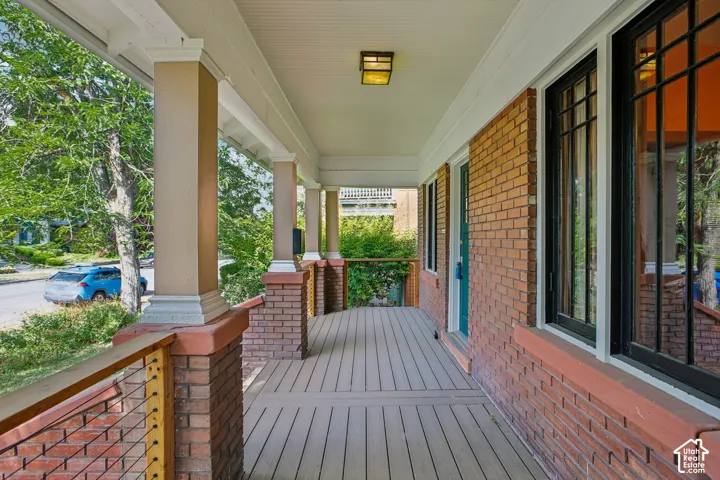 Brick facade with a covered porch featuring wood-finish decking, decorative pillars, and a cable railing system