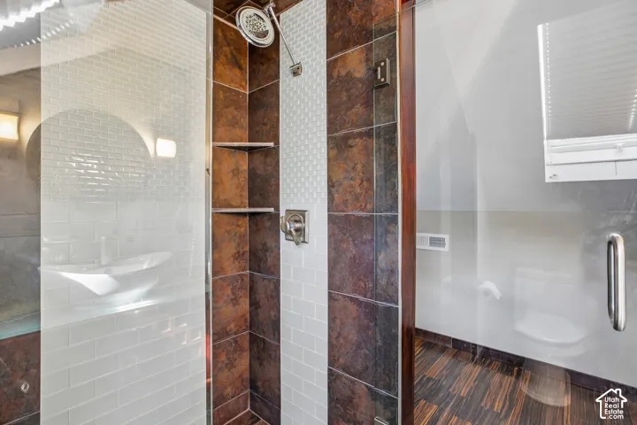 Shower enclosure featuring a glass door, rain showerhead, built-in corner shelving, and contrasting tile finishes