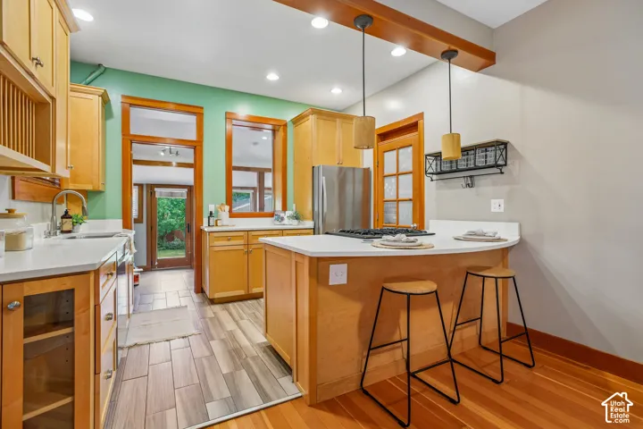 Kitchen featuring wood-finish cabinetry, white countertops, stainless steel appliances, a breakfast bar, and mixed-material flooring