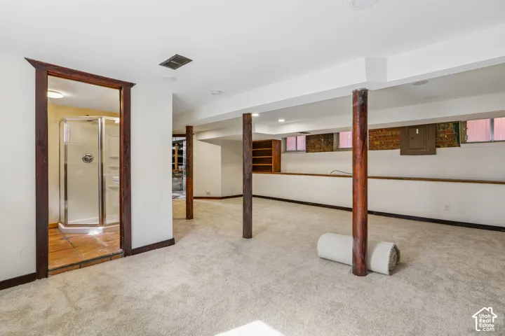 Expansive room featuring recessed lighting, light-toned carpeting, wood support columns, and an adjacent room with a glass-enclosed shower