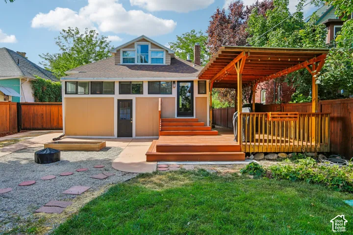 Expansive backyard featuring a wood deck with pergola, gravel patio with stepping stones, and manicured lawn