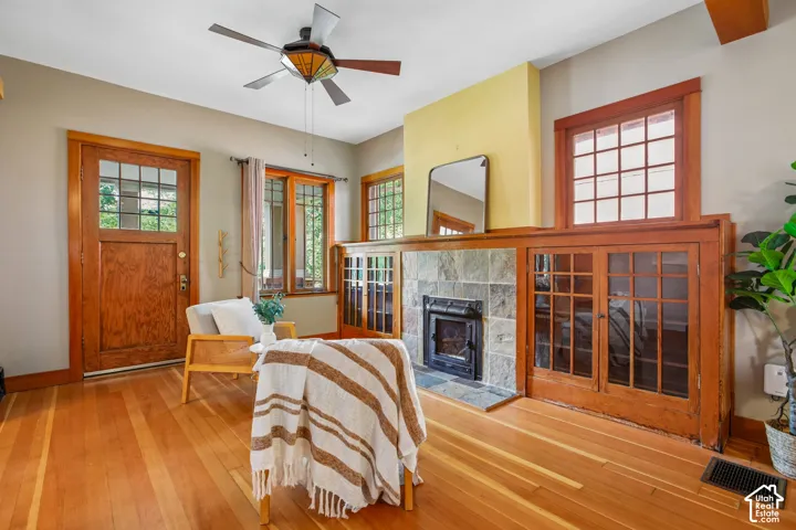 Hardwood flooring, wood-framed windows, wood-paneled door with glass inserts, stone-clad fireplace, and built-in wood cabinetry