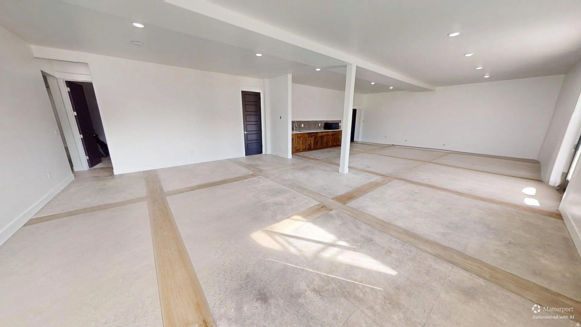 Expansive open-concept space featuring light-colored flooring with wood-finish accents, recessed lighting, and white walls