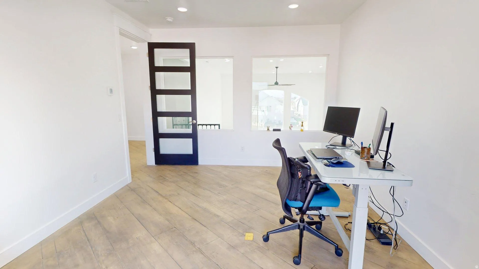 Light wood-finish flooring, white walls, recessed ceiling lighting, and a dark-framed sliding door with glass panels