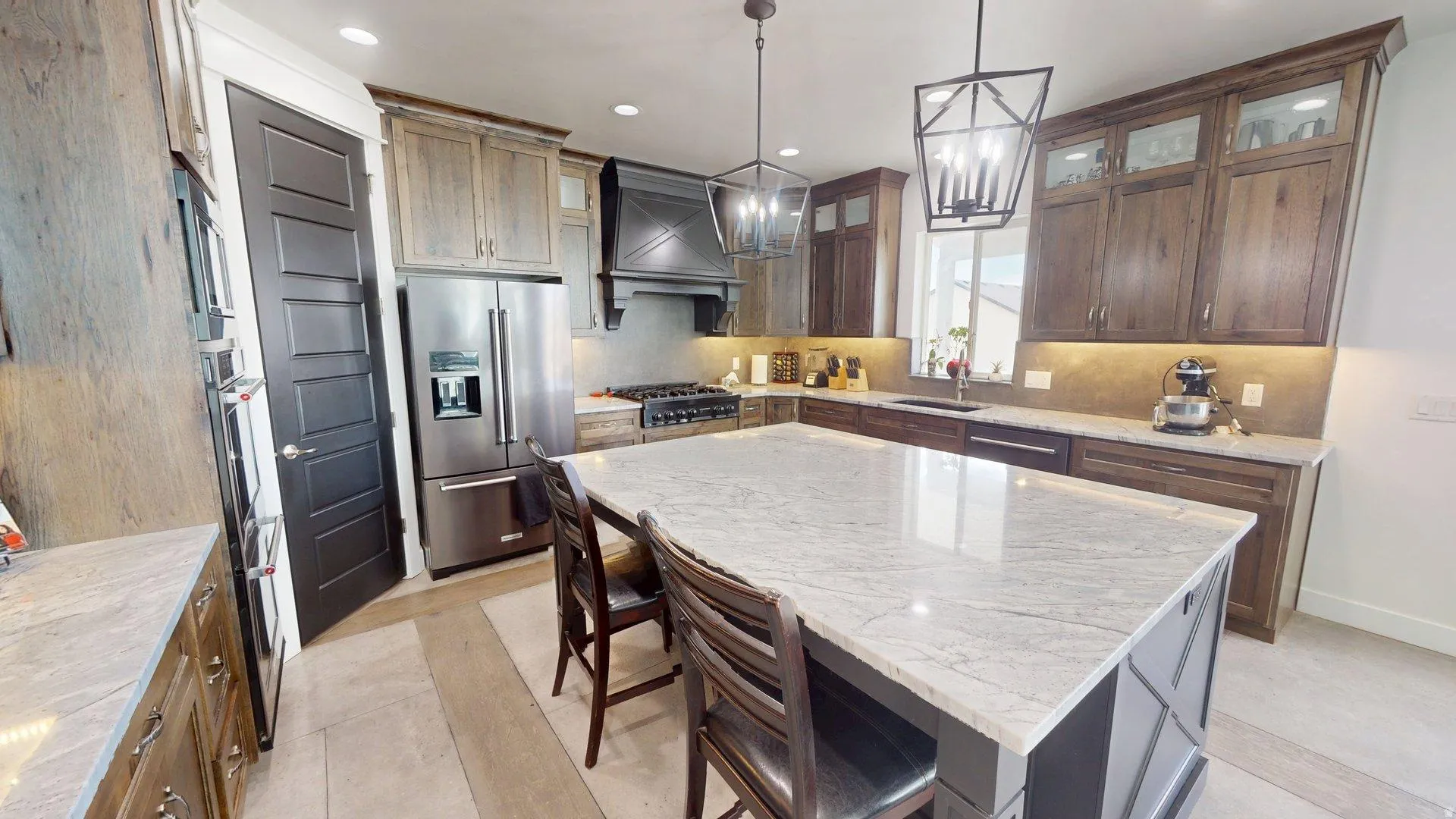 Expansive island with light-toned countertop, stainless steel appliances, dark wood-finish cabinetry with glass inserts, and pendant lighting