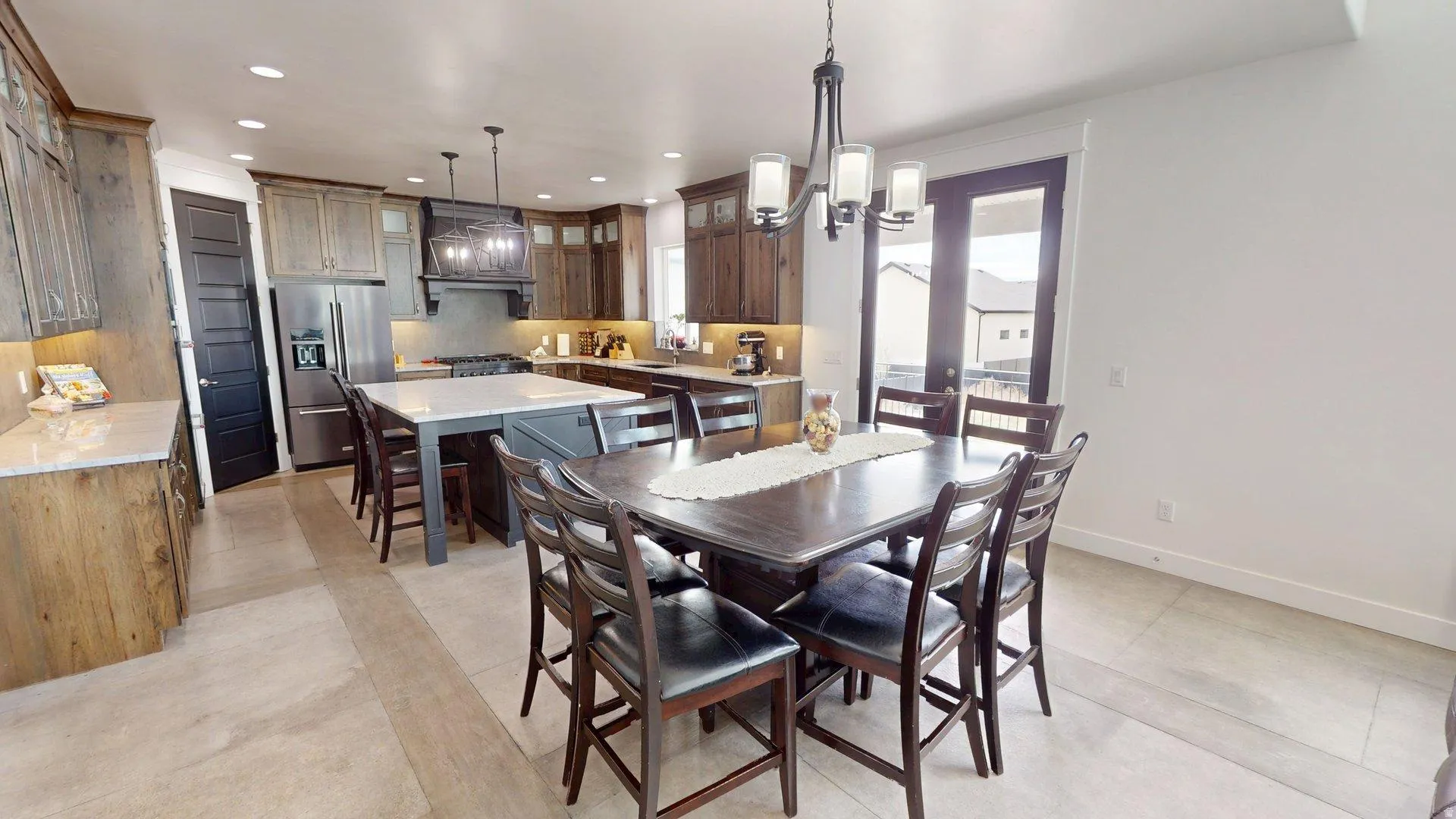 Open-concept kitchen and dining area featuring a large center island, stainless steel appliances, dark wood cabinetry, light tile flooring, and French doors