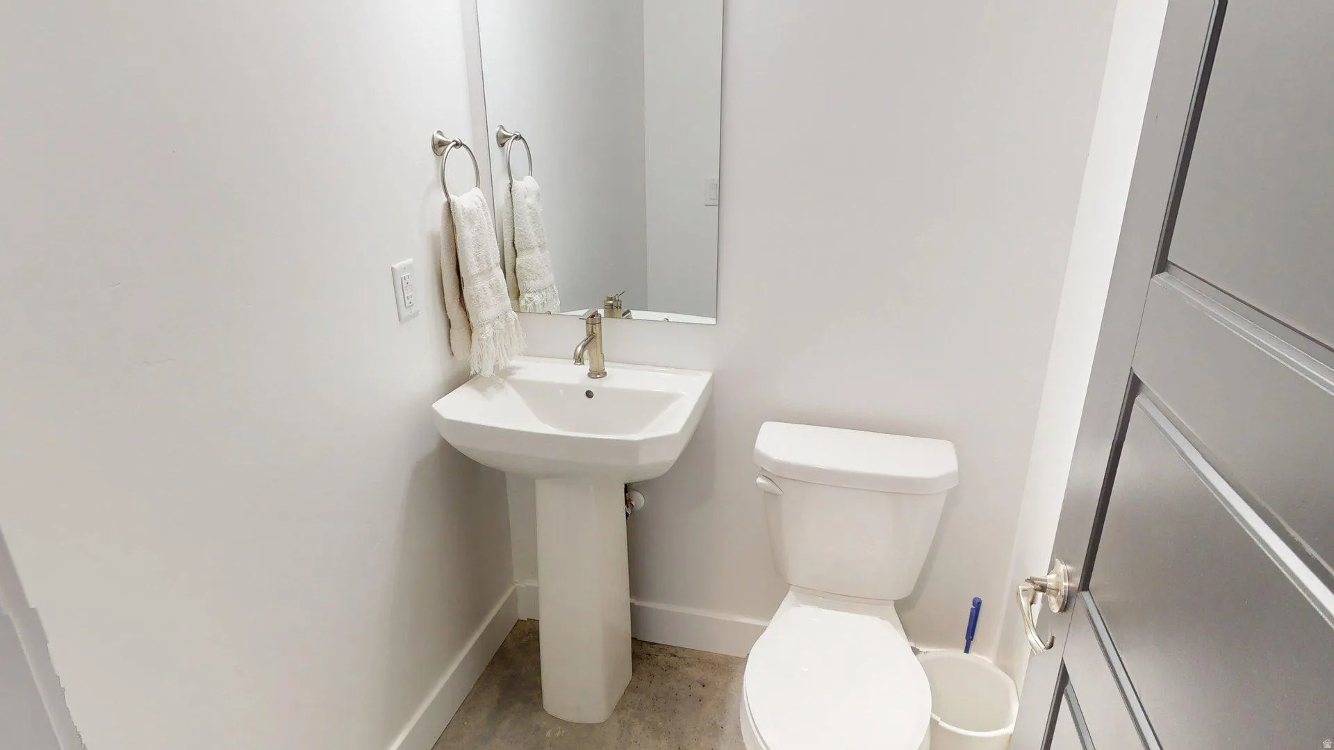 Pedestal sink with a single-handle faucet, wall-mounted mirror, and white toilet