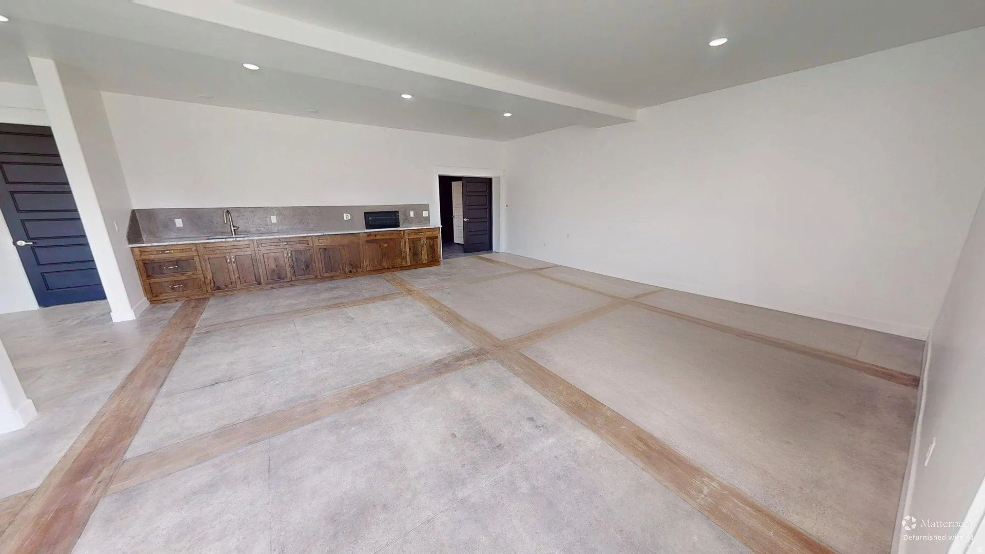 Spacious room featuring concrete flooring with decorative wood-look inlays, a built-in wet bar with wood cabinetry, and recessed lighting
