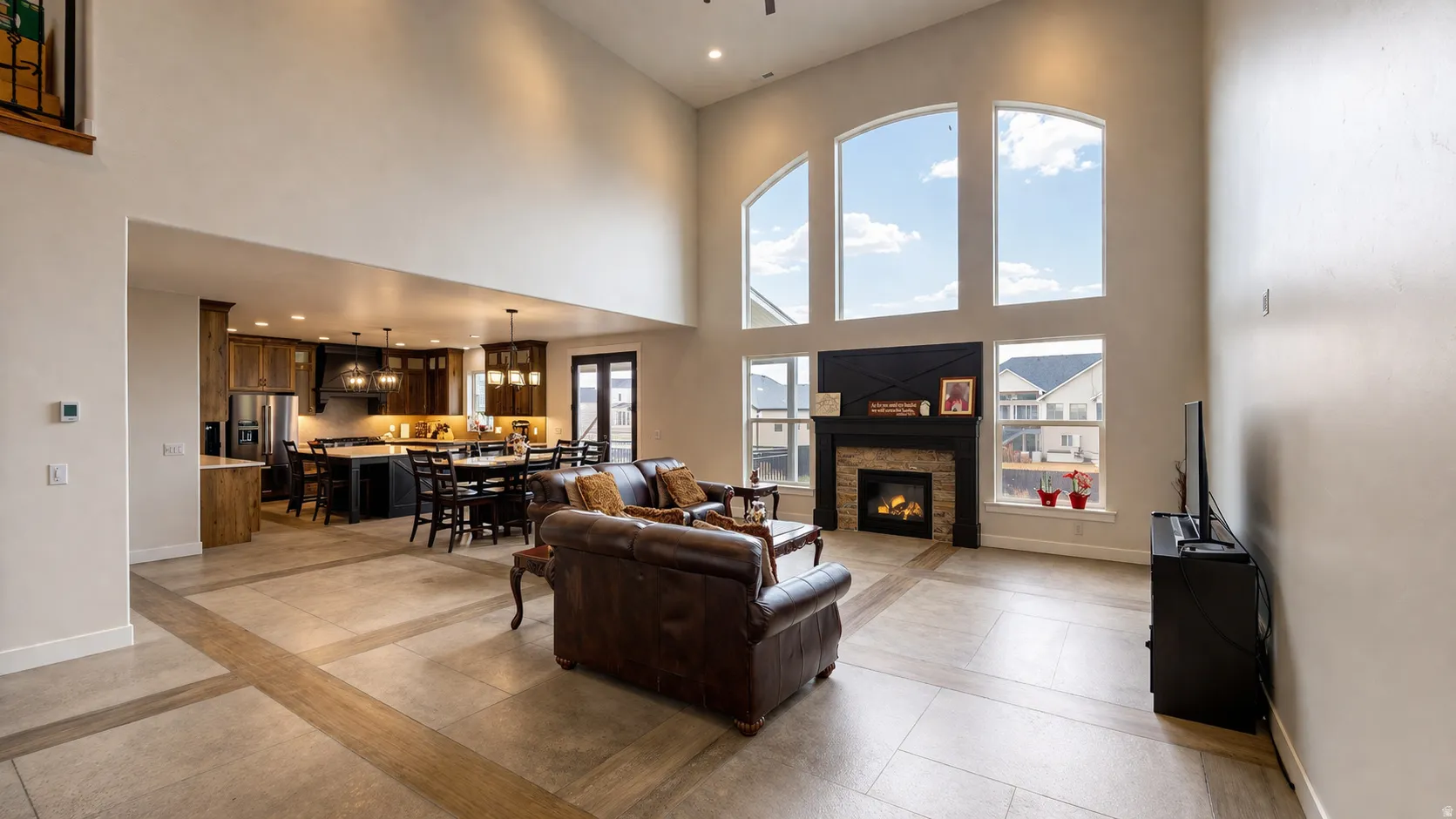 Vaulted ceiling living area with large arched windows, stone-clad fireplace, and tile flooring