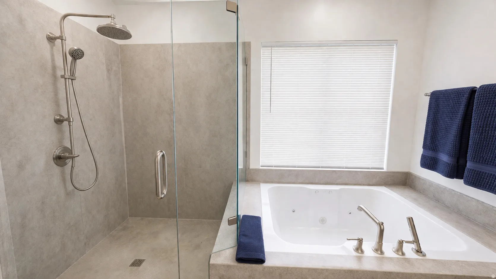 Spa-inspired primary bathroom featuring a frameless glass-enclosed shower with rainfall showerhead and hand-held spray, a freestanding soakable bathtub with deck-mounted faucet, neutral stone-look tile finishes, and a large operable window providing natur