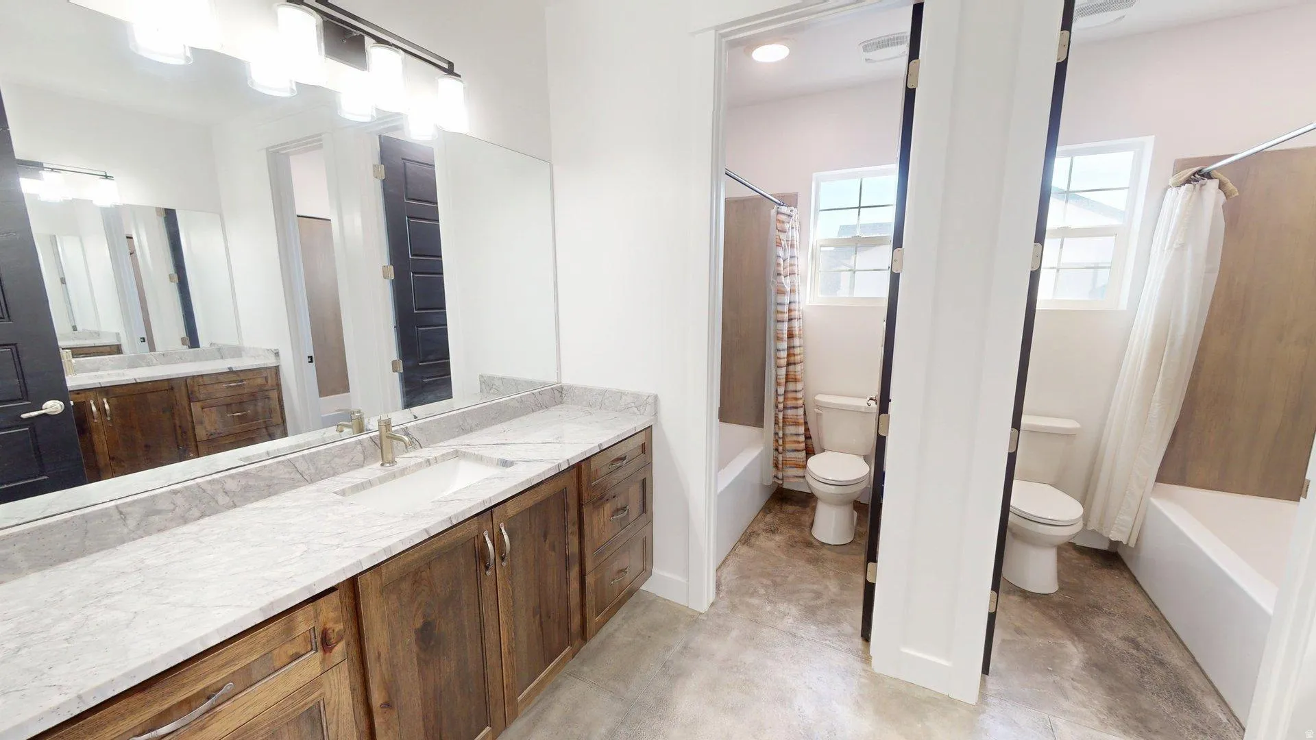 Dual vanity with stone countertops and brass fixtures, complemented by two separate water closets with windows