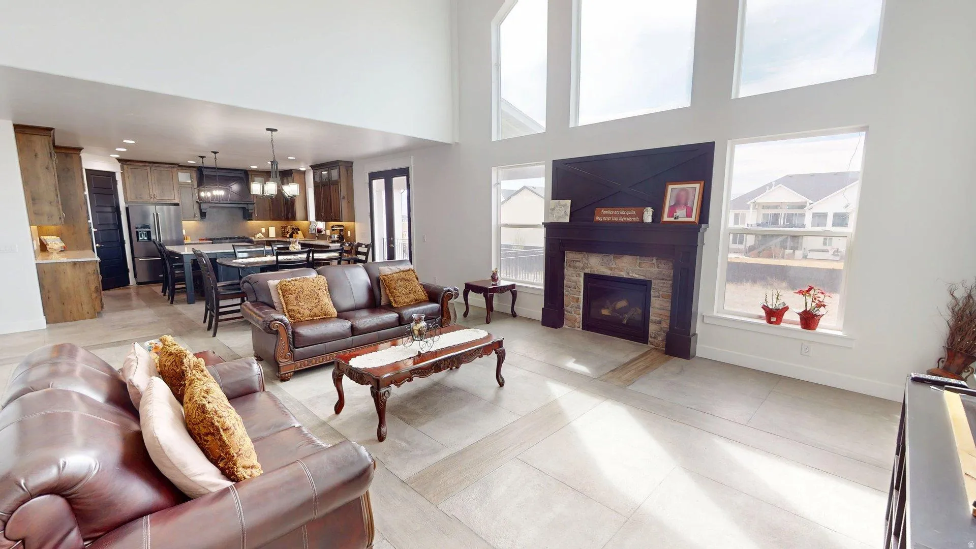 Vaulted ceilings with expansive windows, stone-surround fireplace with dark wood mantel, open-concept kitchen with dark cabinetry, large kitchen island with seating, and wood-finish flooring