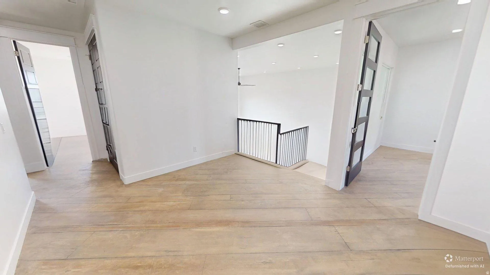 Wide plank wood-finish flooring, recessed lighting, white walls, black metal railing, and black-framed doors with frosted panels