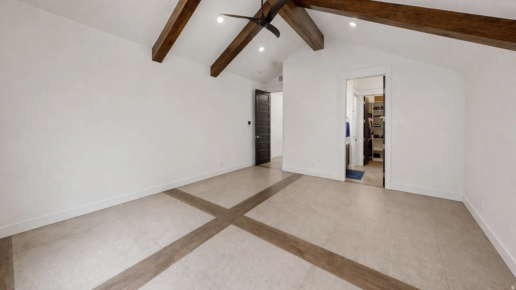 Vaulted ceiling with exposed wood beams, ceiling fan, recessed lighting, tile flooring with wood-finish inlay, and a dark-paneled door