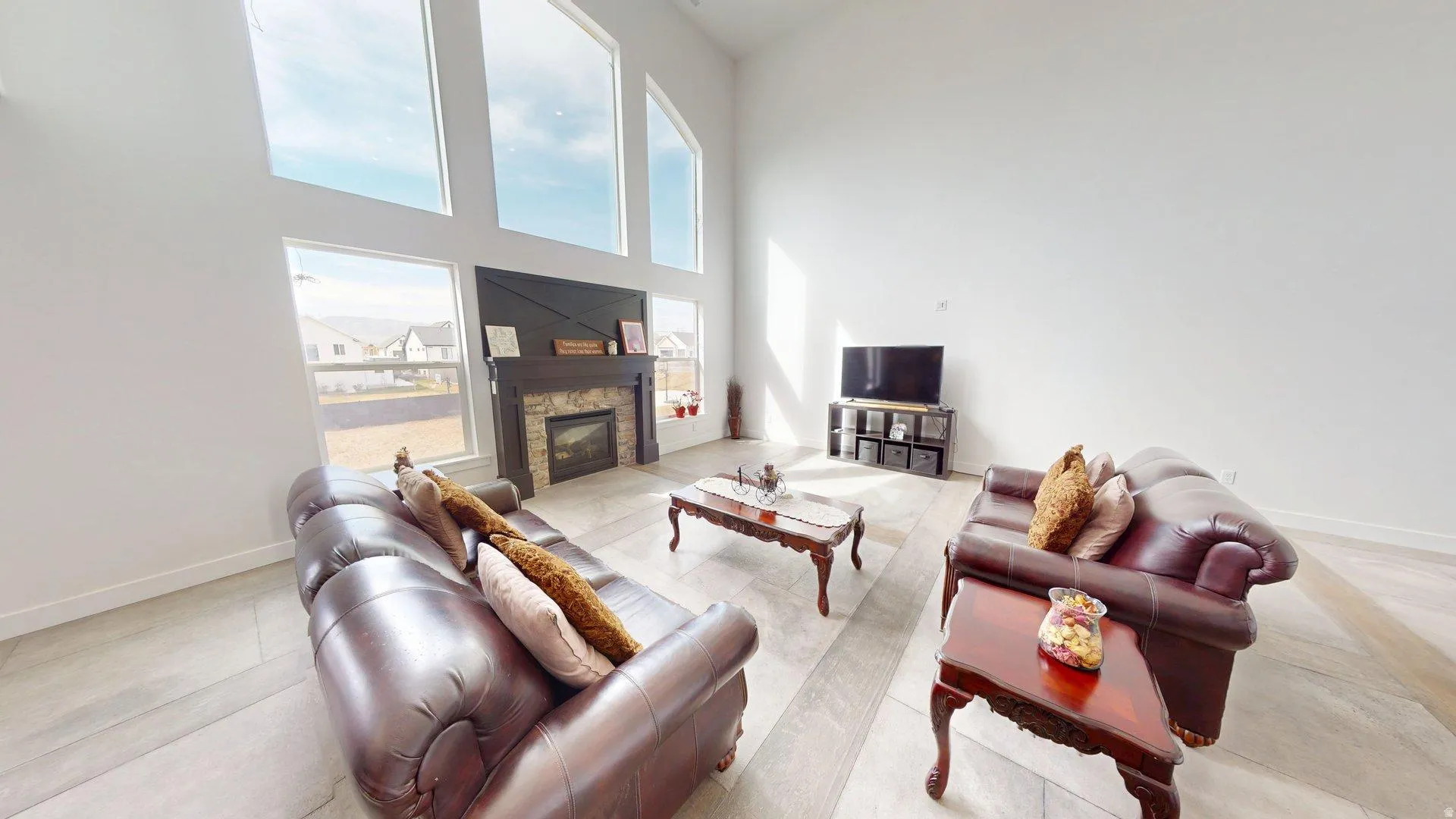 Vaulted ceilings with expansive windows, stone-clad fireplace with wood mantel, and wood-finish flooring