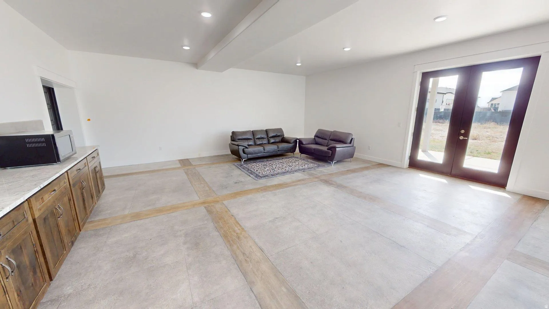 Spacious room with concrete flooring featuring wood-finish accents, recessed lighting, built-in cabinetry with a stone countertop, and double glass-paneled doors