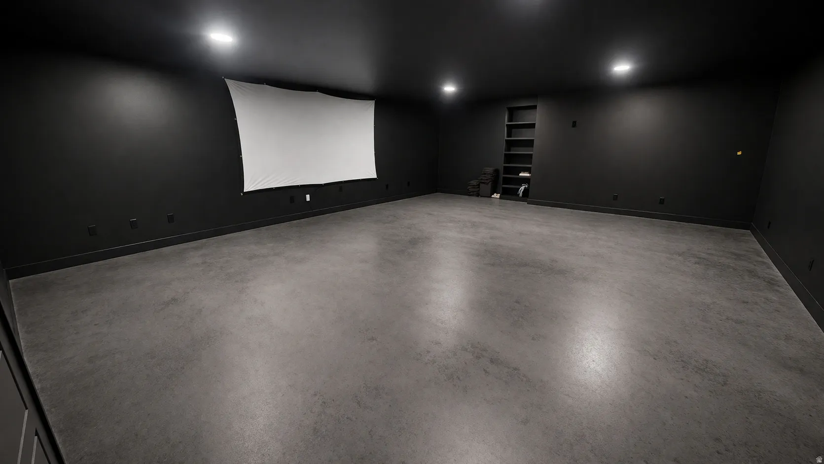 Expansive room featuring dark-painted walls, a large projection screen, recessed ceiling lighting, built-in shelving, and polished concrete flooring
