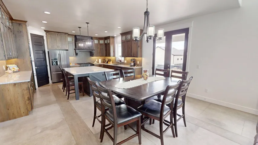 Open-concept kitchen and dining area featuring a large center island, stainless steel appliances, dark wood cabinetry, light tile flooring, and French doors