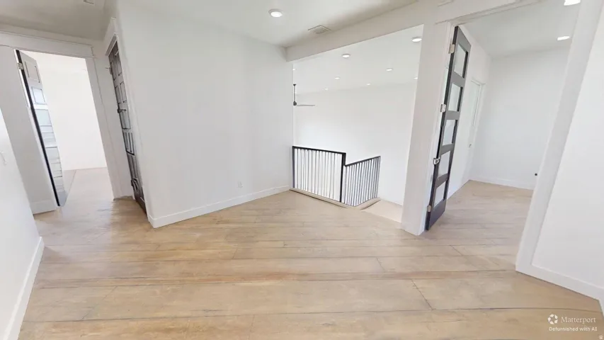 Wide plank wood-finish flooring, recessed lighting, white walls, black metal railing, and black-framed doors with frosted panels