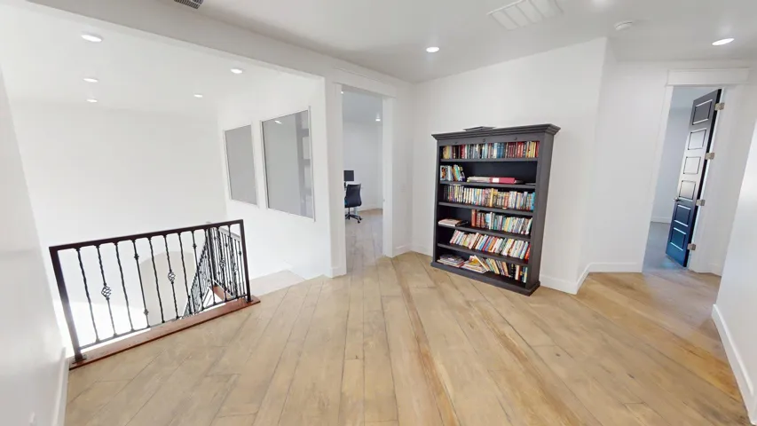 Hardwood flooring, recessed lighting, white walls, dark iron railing, and a dark paneled door
