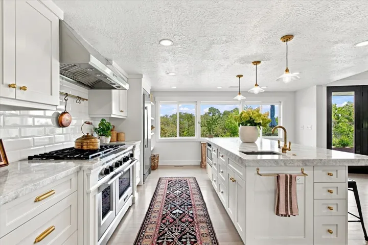 Gourmet kitchen featuring white cabinetry, marble countertops, professional-style gas range, and oversized island.