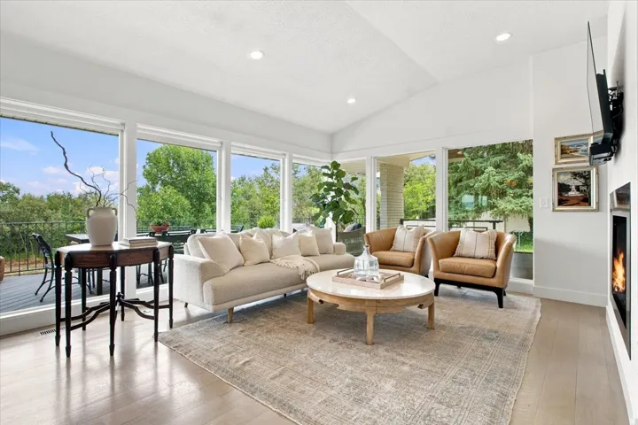 Light-filled great room with vaulted ceilings, hardwood floors, contemporary fireplace, and walls of windows overlooking the property.