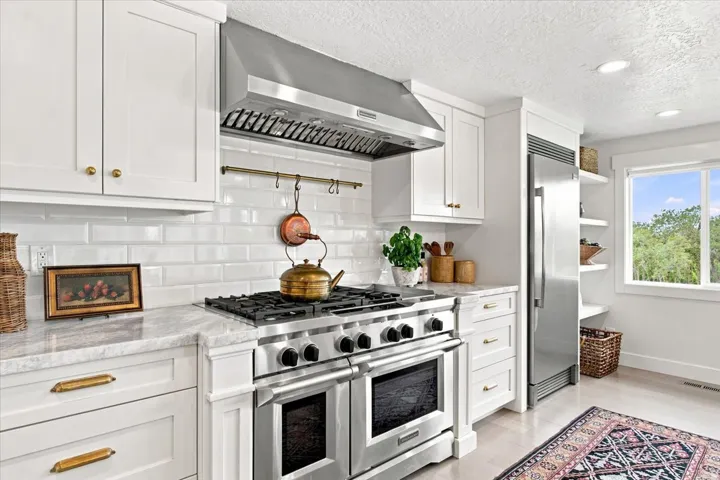 Professional-style gas range with custom hood, white cabinetry, and timeless subway tile backsplash.