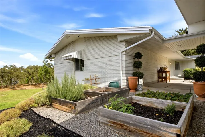 Charming garden area with raised beds and covered patio space surrounded by mature landscaping.
