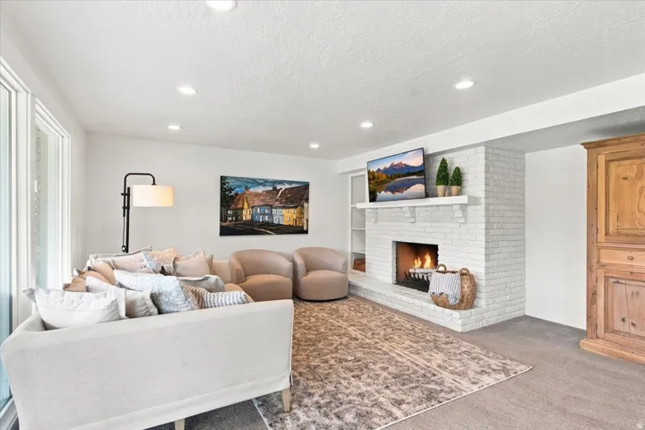 Finished lower-level family room with white brick fireplace, recessed lighting, and oversized windows.