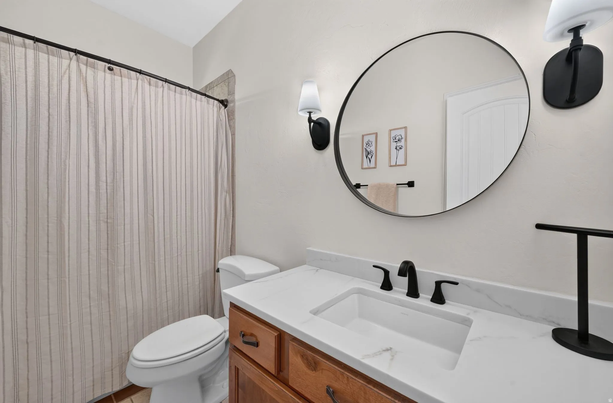 Wood-finish vanity with white countertop, undermount sink, matte black faucet, and circular wall mirror
