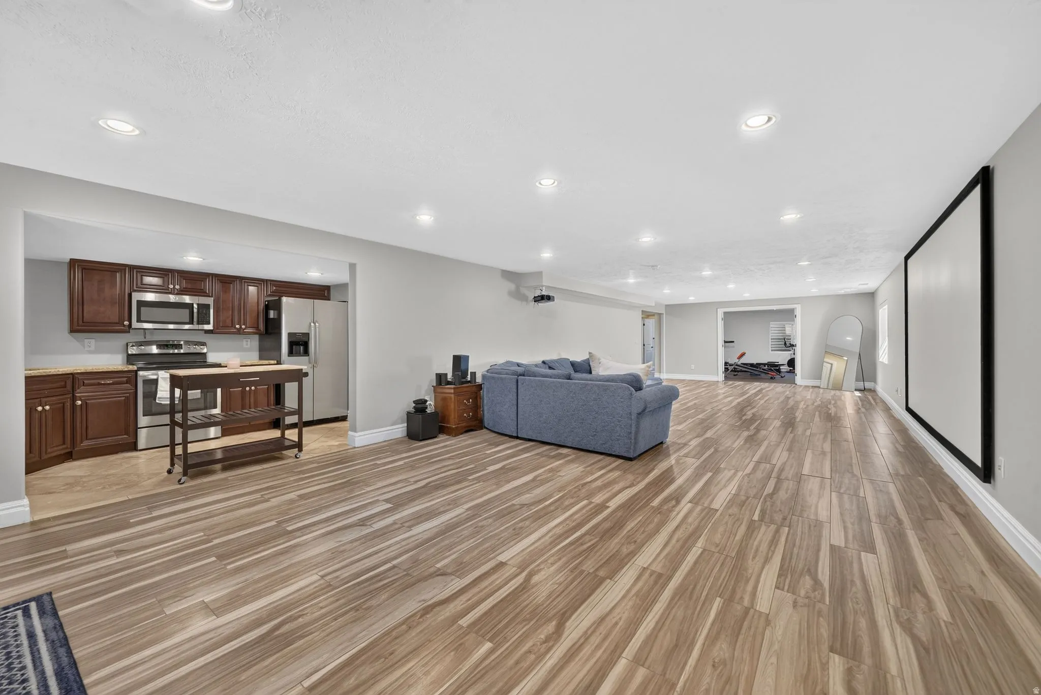 Spacious open-concept area featuring wood-finish flooring, recessed lighting, and a large wall-mounted screen