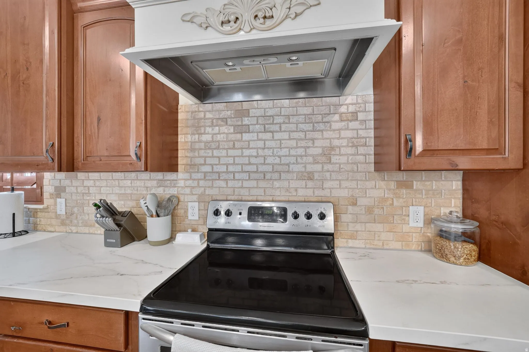 Solid wood cabinetry, decorative range hood with stainless steel insert, subway tile backsplash, stainless steel electric range, and light-colored countertops