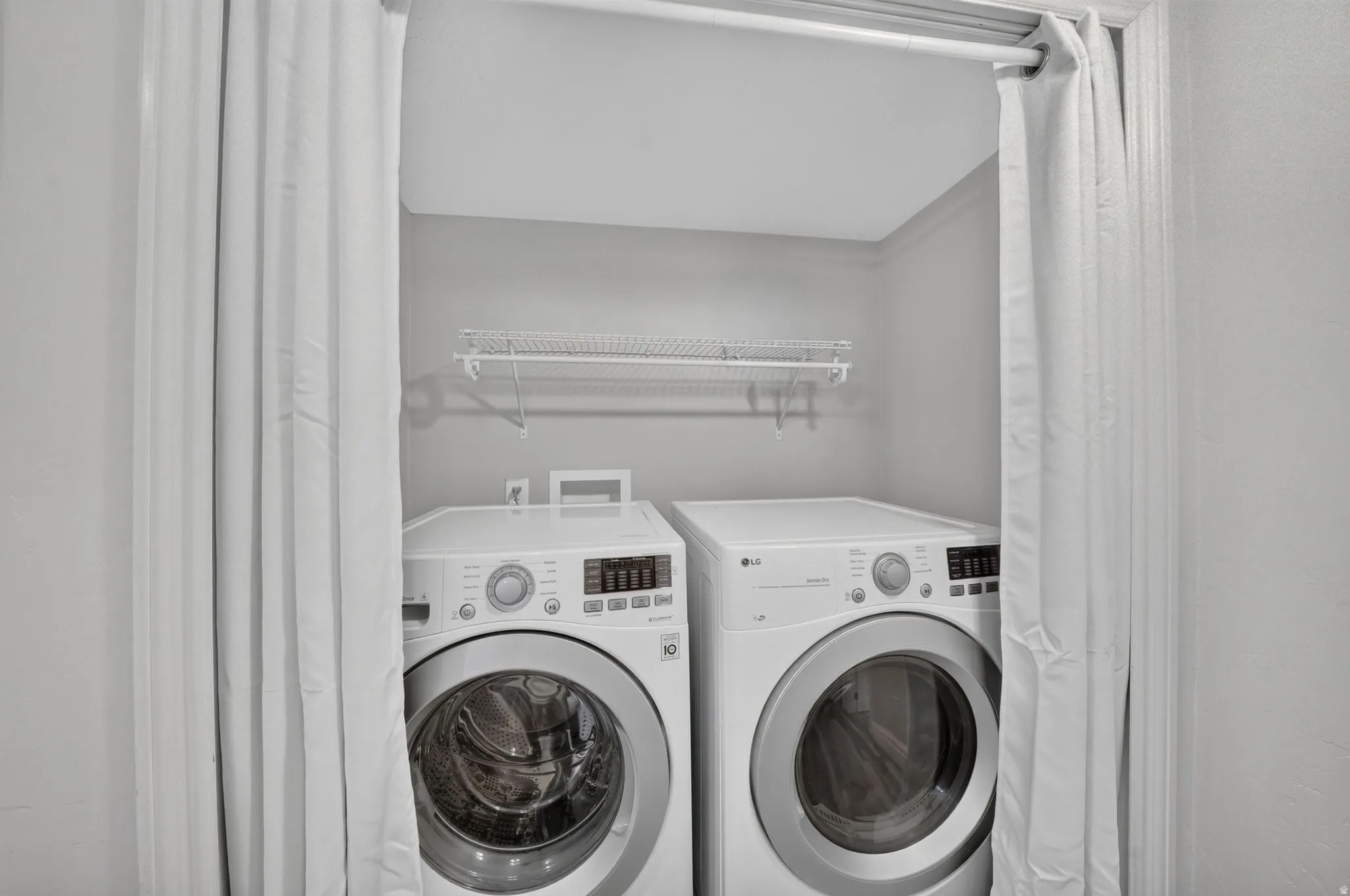 Dedicated laundry area with white front-load washer and dryer, accompanied by a wall-mounted wire shelf for storage