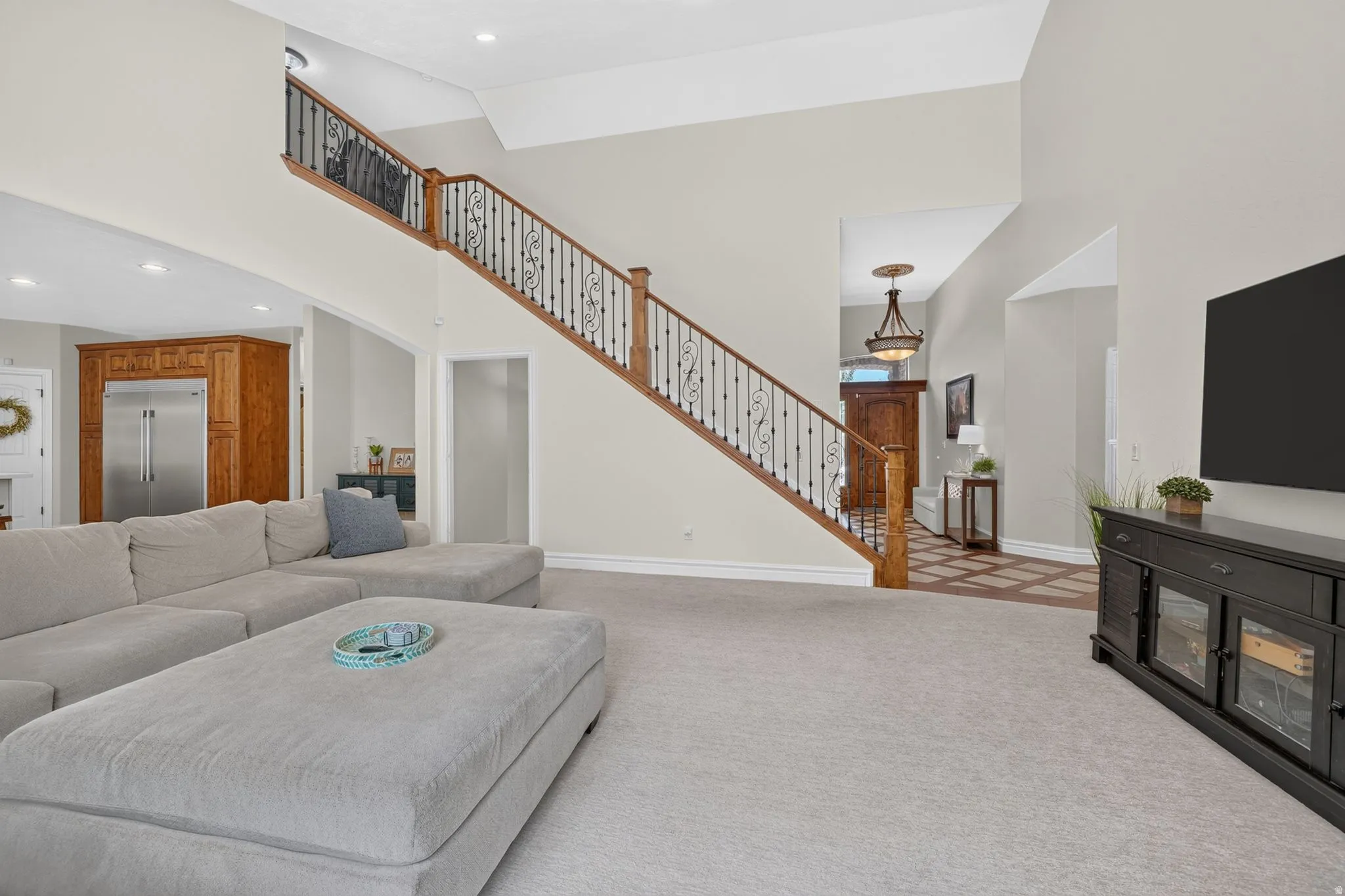 Two-story ceiling, wood staircase with ornate metal balusters, and recessed lighting