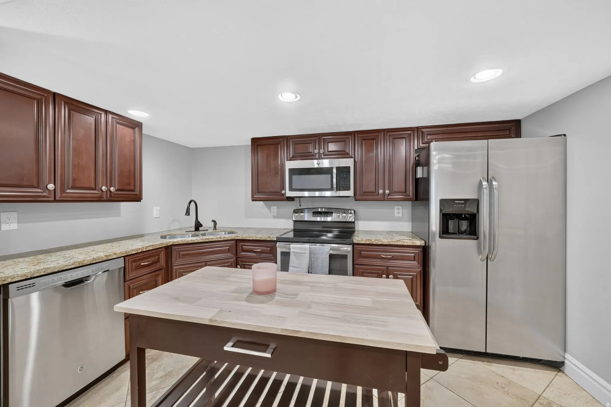 Kitchen featuring stainless steel appliances, wood cabinetry, stone countertops, and a central island