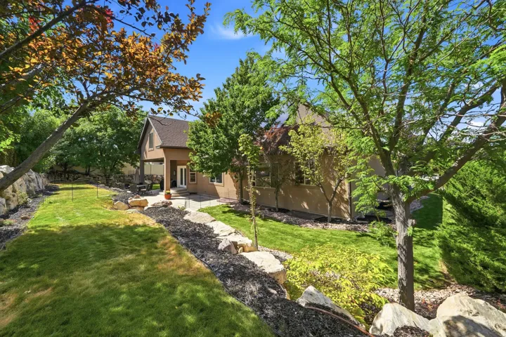 Expansive backyard featuring a stone patio, covered outdoor living space, natural rock retaining walls, and mature landscaping