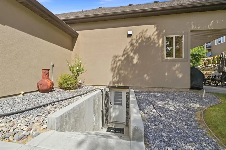 Exterior stucco finish, concrete basement entryway, gravel landscaping, and a dual-pane window
