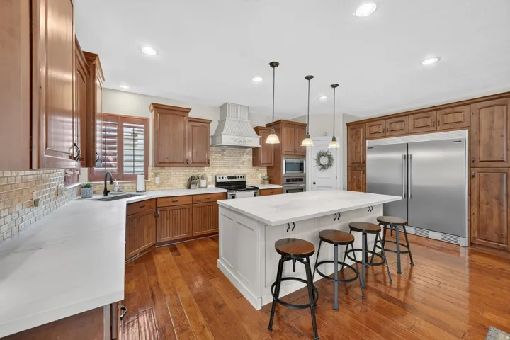 Spacious kitchen featuring a large central island with seating, extensive wood cabinetry, stainless steel appliances, and wood-finish flooring