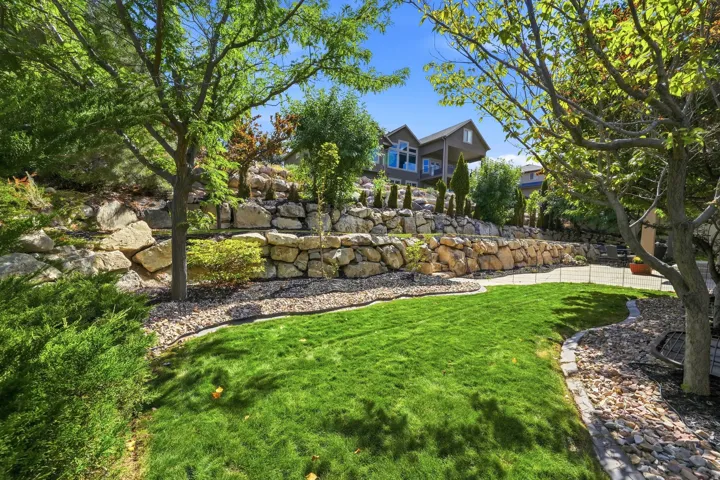 Sloped landscaping featuring multiple rock retaining walls, terraced lawn areas, and mature trees