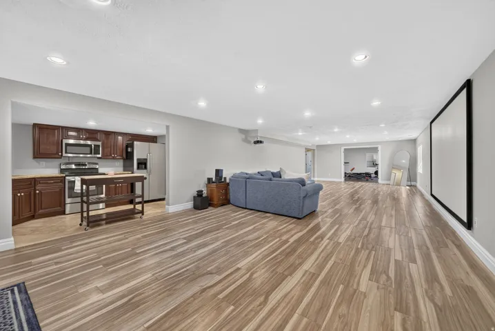 Spacious open-concept area featuring wood-finish flooring, recessed lighting, and a large wall-mounted screen