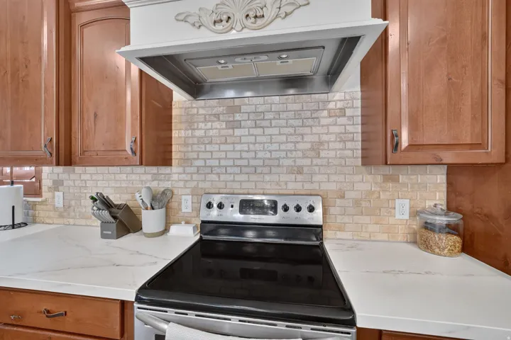 Solid wood cabinetry, decorative range hood with stainless steel insert, subway tile backsplash, stainless steel electric range, and light-colored countertops