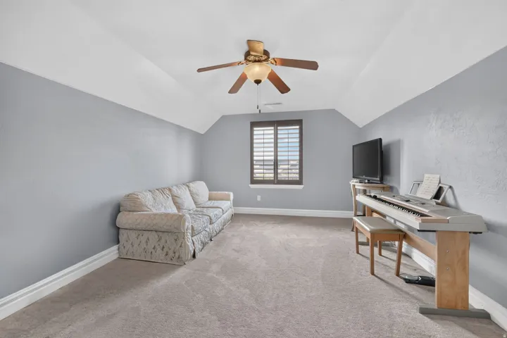 Carpeted room featuring a ceiling fan, a window with plantation shutters, and sloped ceilings